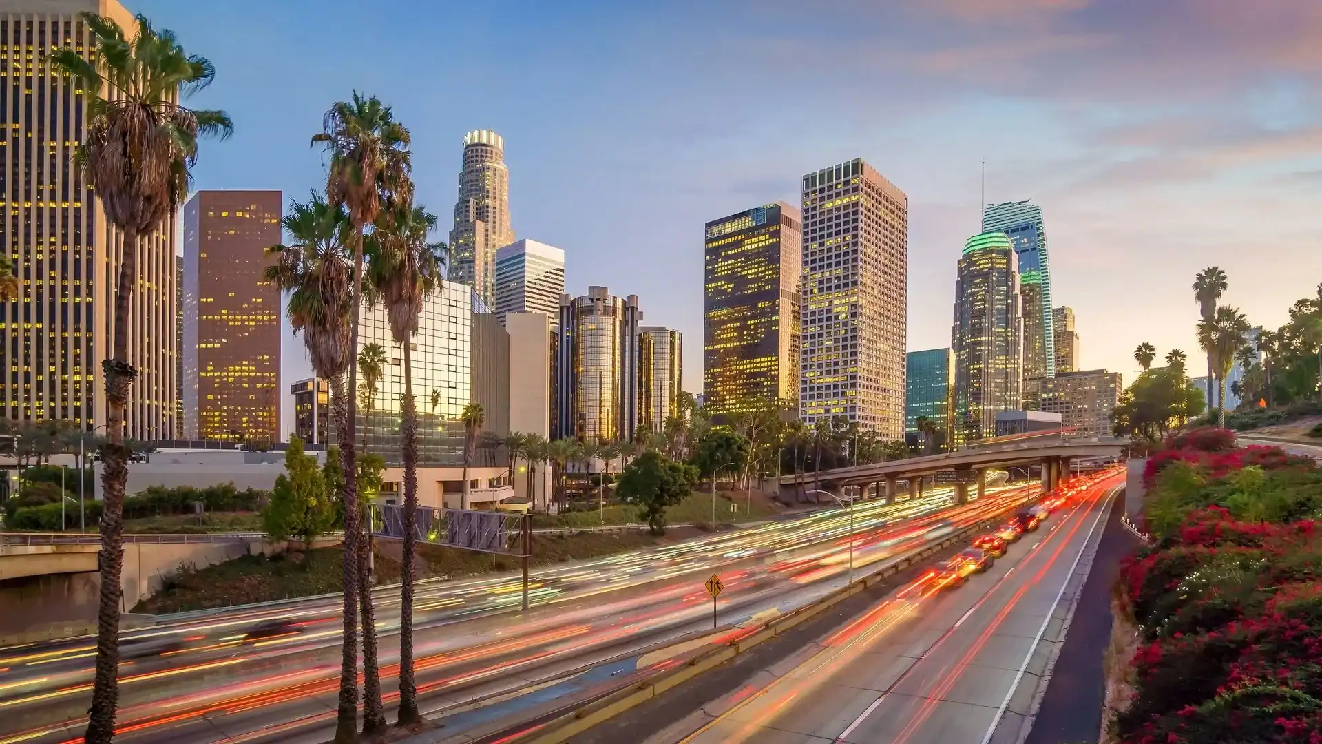 Downtown Los Angeles cityscape with tall buildings, palm trees, and blurred lights of cars on a busy freeway at dusk—perfect for stunning balloon installations.