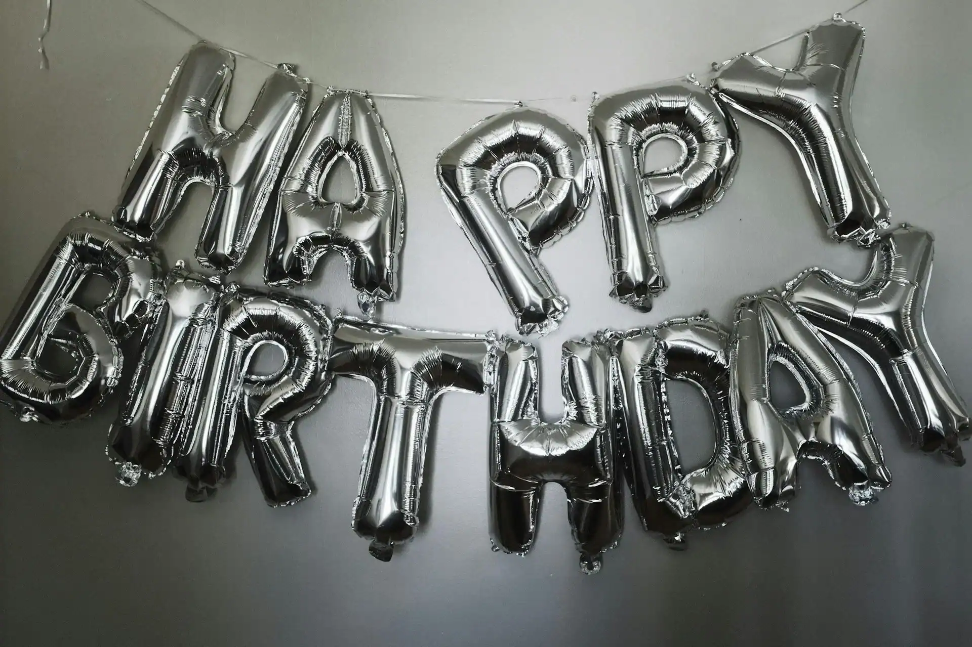 Silver foil balloons spell "Happy Birthday" and are hung on a wall, creating eye-catching balloon decor perfect for birthday celebrations in Los Angeles.
