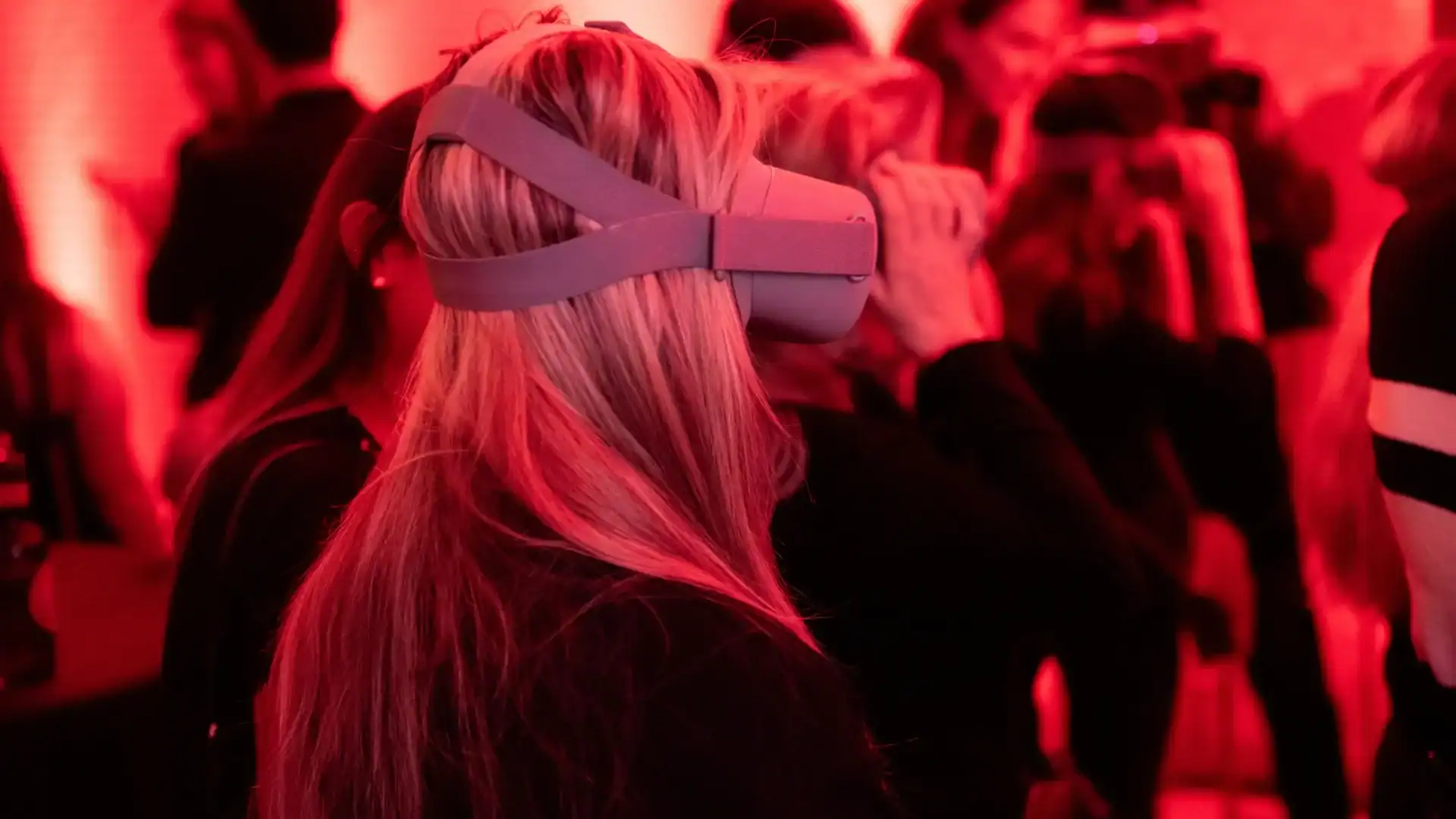 A group of people in a dimly lit red room in Los Angeles wear virtual reality headsets, focusing on their immersive experience amid striking balloon installations.