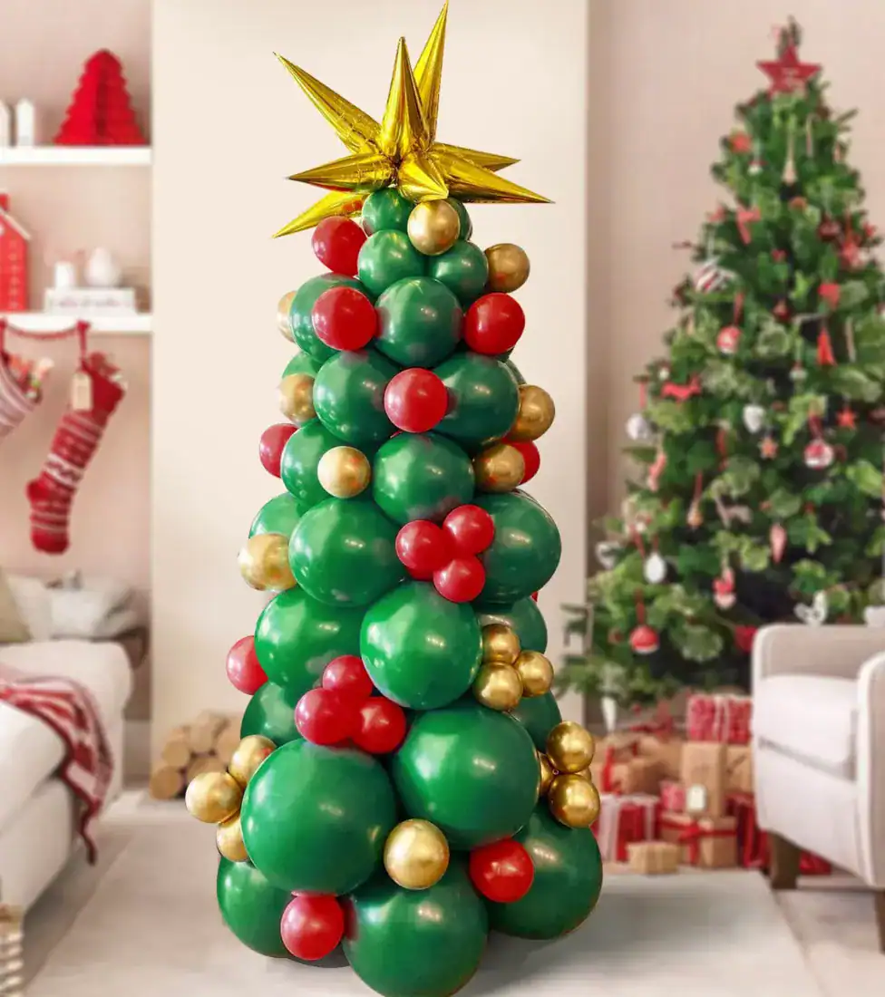 A Christmas tree-shaped balloon arrangement by a talented Los Angeles balloon artist features green, red, and gold balloons, standing in a living room beside a decorated Christmas tree and festive holiday decor.