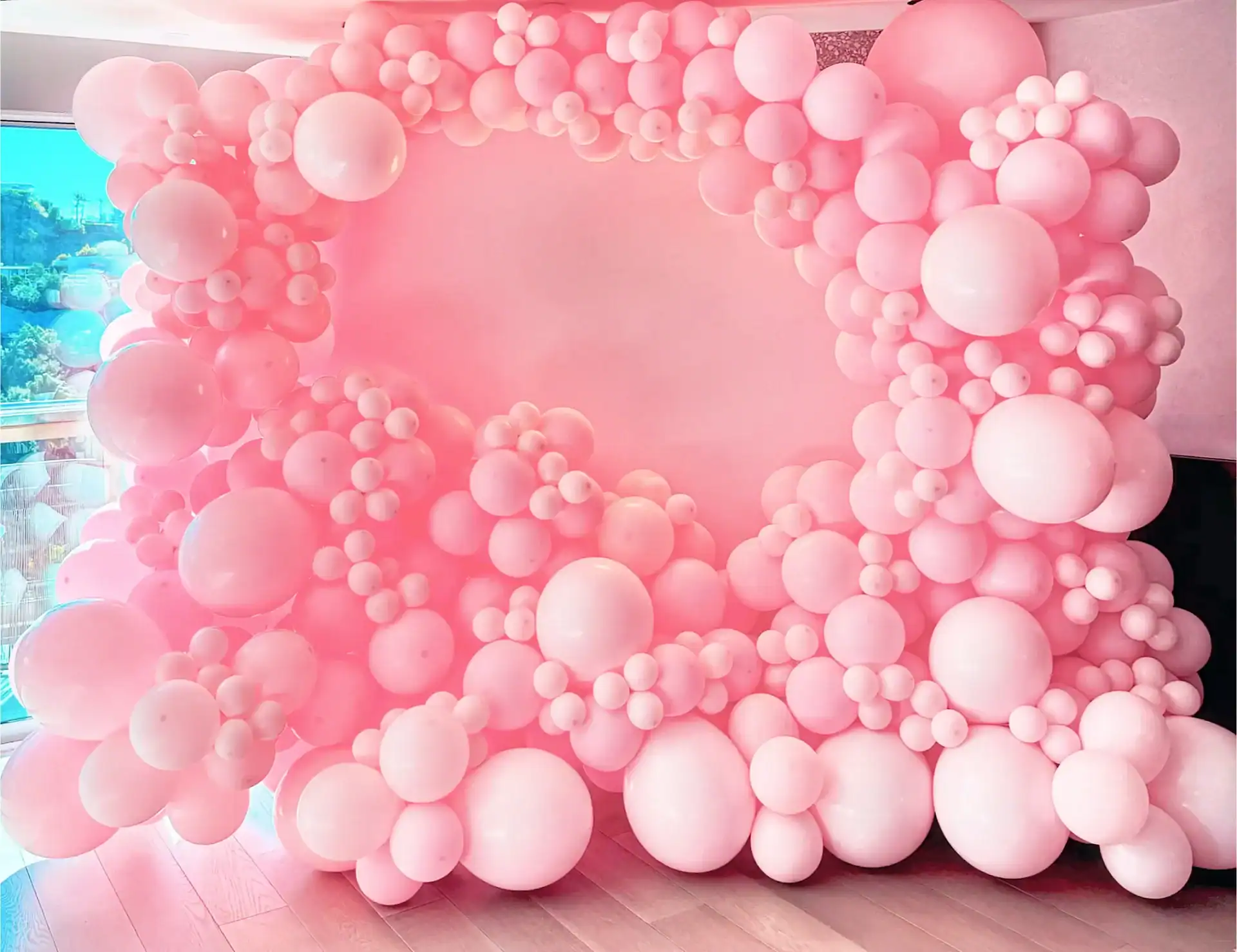 A large decorative pink balloon arch installation featuring various sizes of balloons, arranged indoors near a window—perfect for making a statement at your next corporate event.