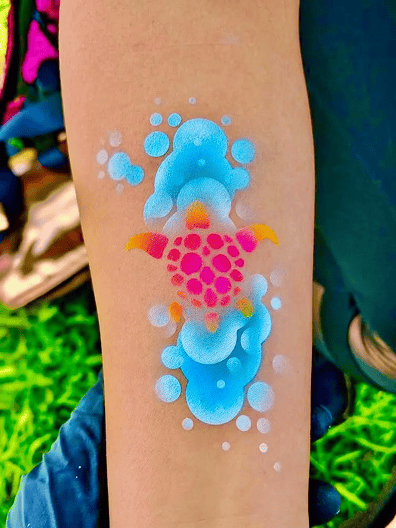 A colorful turtle design surrounded by blue and white bubbles, reminiscent of trendy balloon decor, is painted on a person's forearm.