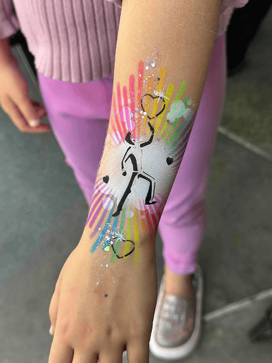 A forearm with colorful face paint featuring abstract rainbow lines, a black stick figure playing soccer, and balloon decor details perfect for a corporate event.