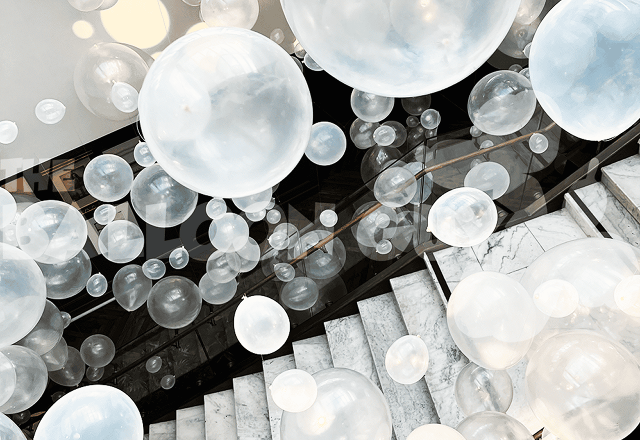 White translucent balloon installations of various sizes float above a marble staircase, creating a layered, airy effect in this modern Los Angeles indoor setting.
