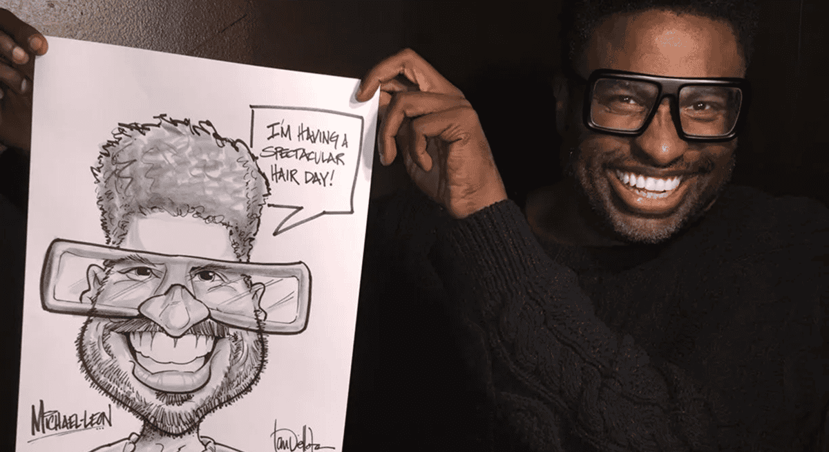 A smiling person at a Los Angeles corporate event holds up a caricature drawing of themselves with exaggerated features and large glasses. The drawing includes a speech bubble saying, "I’m having a spectacular hair day!.
