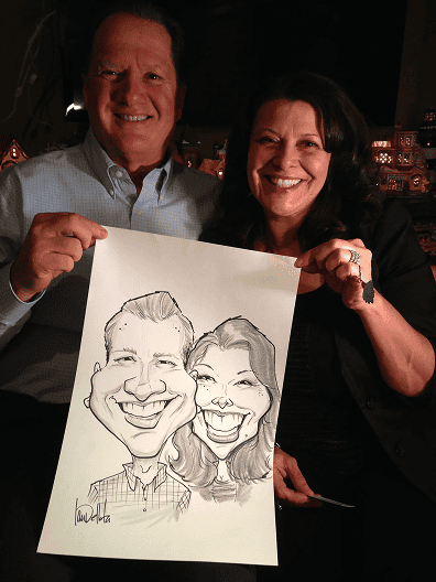 A man and a woman smile while holding up a caricature drawing of themselves at a corporate event in Los Angeles.