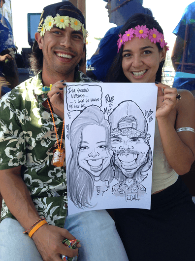 Two people wearing flower headbands and leis smile while holding a caricature drawing of themselves, surrounded by eye-catching balloon installations at an outdoor event.
