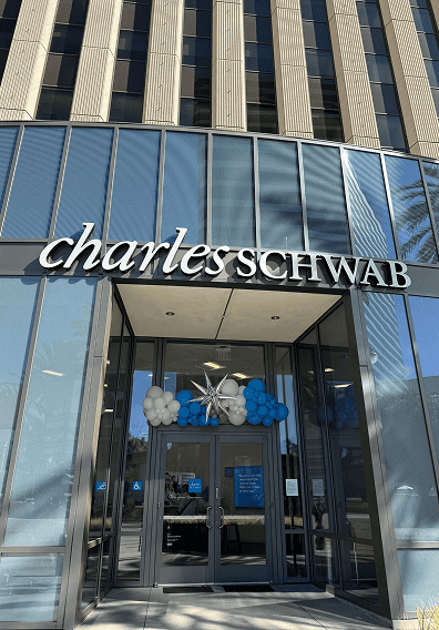 Exterior of a Charles Schwab building in Los Angeles with large glass doors, blue and white balloon installations by a skilled balloon artist above the entrance, and the company name on the facade.