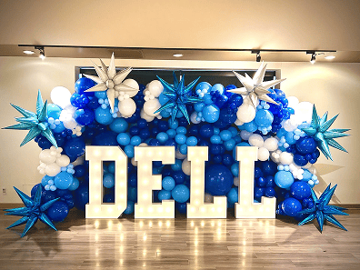 Large illuminated letters spelling "DELL" stand before stunning balloon decor crafted by a skilled balloon artist, featuring blue, white, and silver balloons plus star-shaped accents—an eye-catching setup perfect for Los Angeles events.