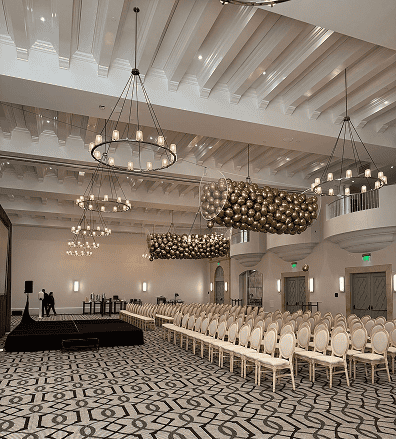 A large, elegant event hall in Los Angeles with rows of beige chairs, patterned carpet, multiple chandeliers, and a stage with audio equipment set up—perfect for adding stunning balloon decor or inviting a talented balloon artist.
