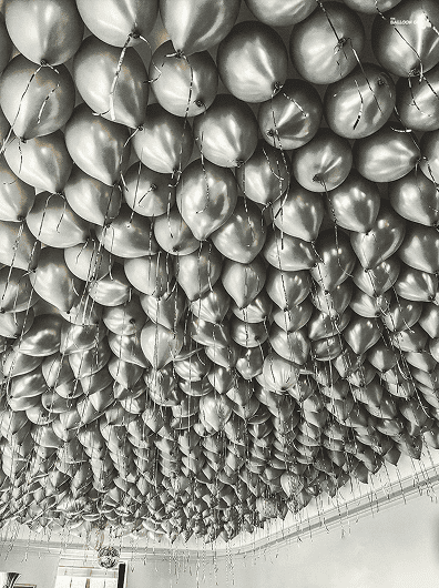 Hundreds of metallic balloons with strings are clustered and floating near the ceiling, creating stunning balloon decor that transforms the entire room.