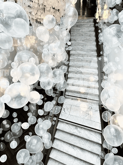 A marble staircase in Los Angeles is decorated with numerous translucent white balloons of various sizes, creating an airy, festive atmosphere.