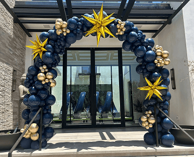 A navy and gold balloon arch with star-shaped decorations stands at the entrance of a modern Los Angeles building, creating striking balloon decor for a corporate event.