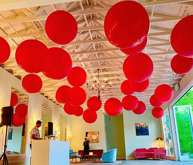 Large red balloon decor hangs from a white open-beam ceiling in a spacious, modern Los Angeles room with seating areas and a chandelier.