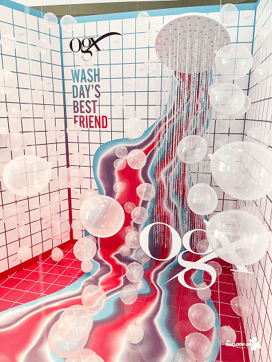 A decorative display in Los Angeles features a large showerhead, white balloons resembling bubbles, and colorful red and blue streaks on a tiled background with "OGX Wash Day's Best Friend" text, highlighting creative balloon installations.