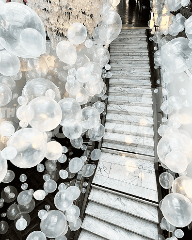 A marble staircase is surrounded by clusters of translucent white balloons, creating a whimsical, airy atmosphere reminiscent of the imaginative balloon installations crafted by a skilled Los Angeles balloon artist.