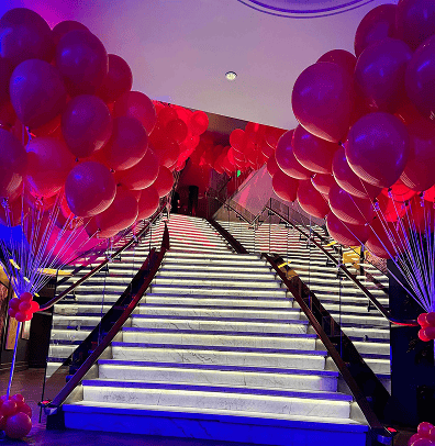 A grand staircase is lined with clusters of red balloon installations on both sides, illuminated by purple and blue lighting.