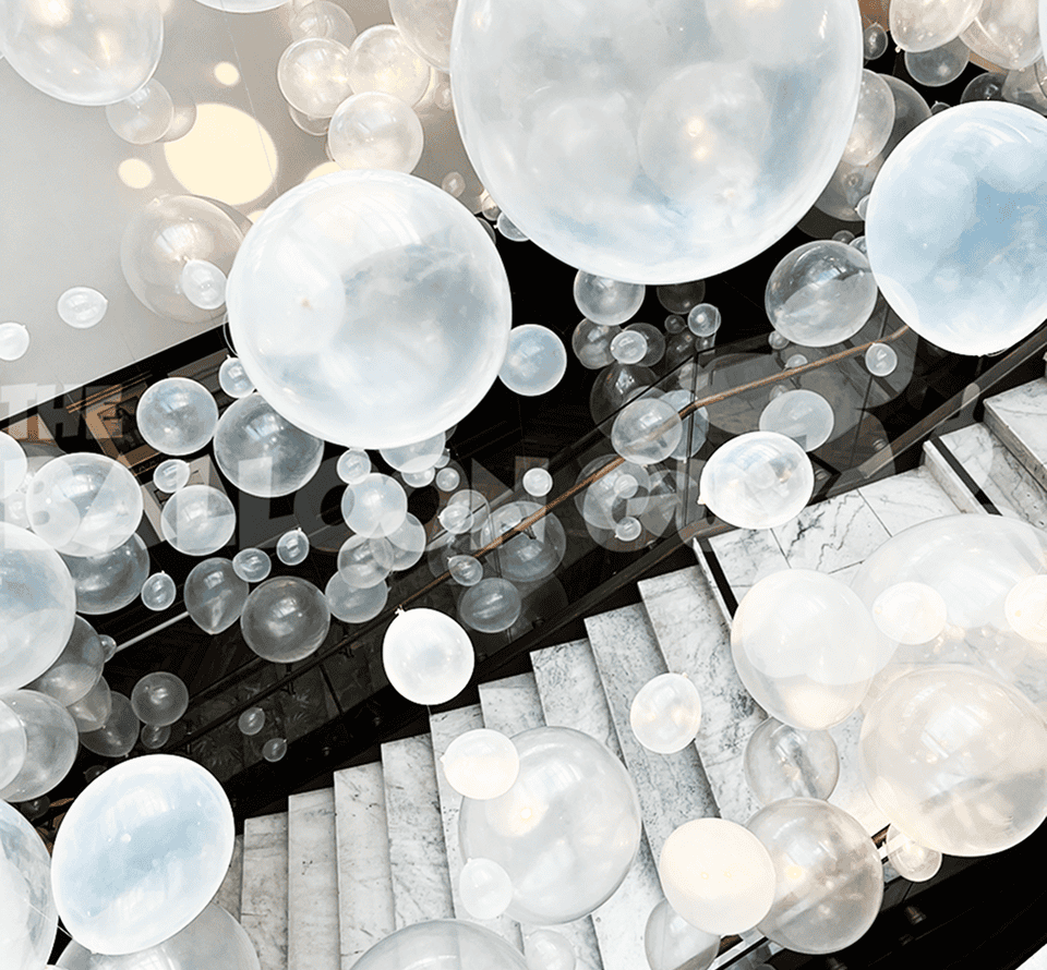 Large, translucent white balloons are suspended above a marble staircase, creating a floating effect in this modern Los Angeles corporate event setting.