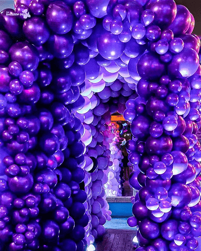 A tunnel-like archway made of various sizes of purple and lavender balloons, leading to a vibrant, balloon-filled room—perfect for creative balloon installations at your next corporate event in Los Angeles.