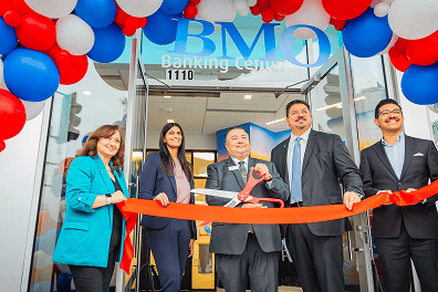 Five people stand in front of a BMO Banking Center in Los Angeles, cutting a red ribbon under striking red, white, and blue balloon installations at a grand opening corporate event.