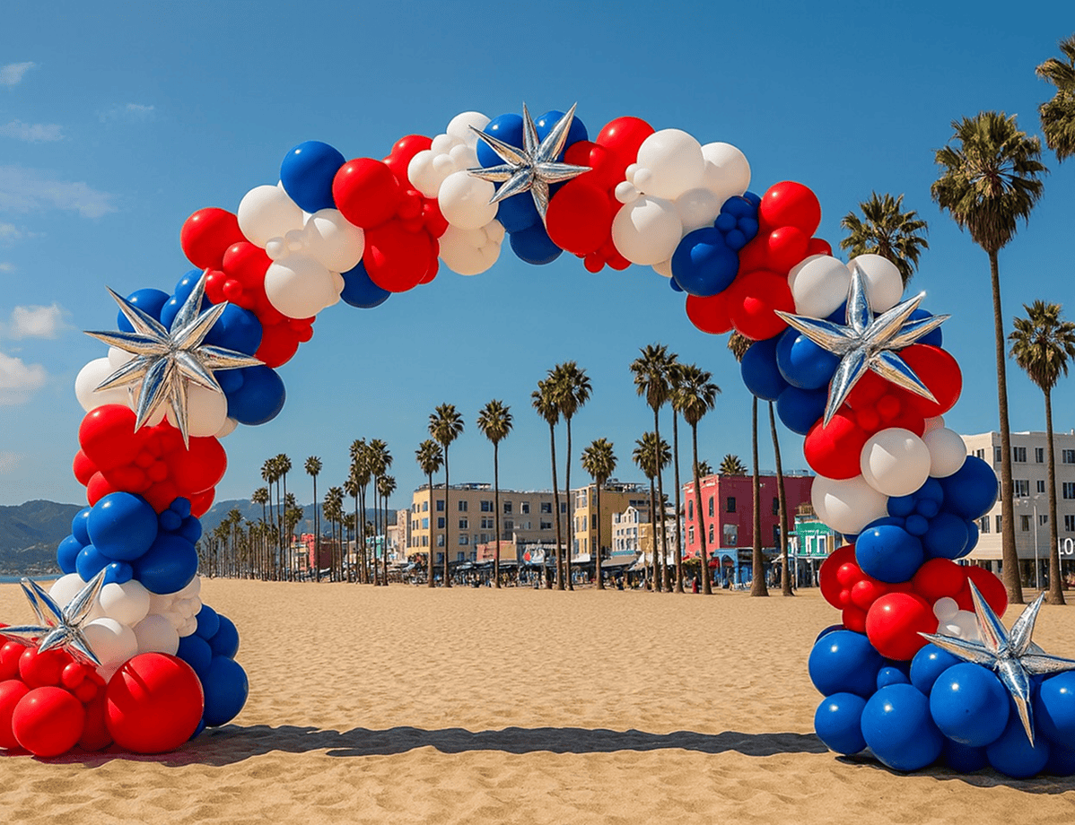 A large arch made of red, white, and blue balloons with silver star decorations stands on a sandy Los Angeles beach, surrounded by palm trees and colorful buildings—an eye-catching balloon installation perfect for a corporate event.