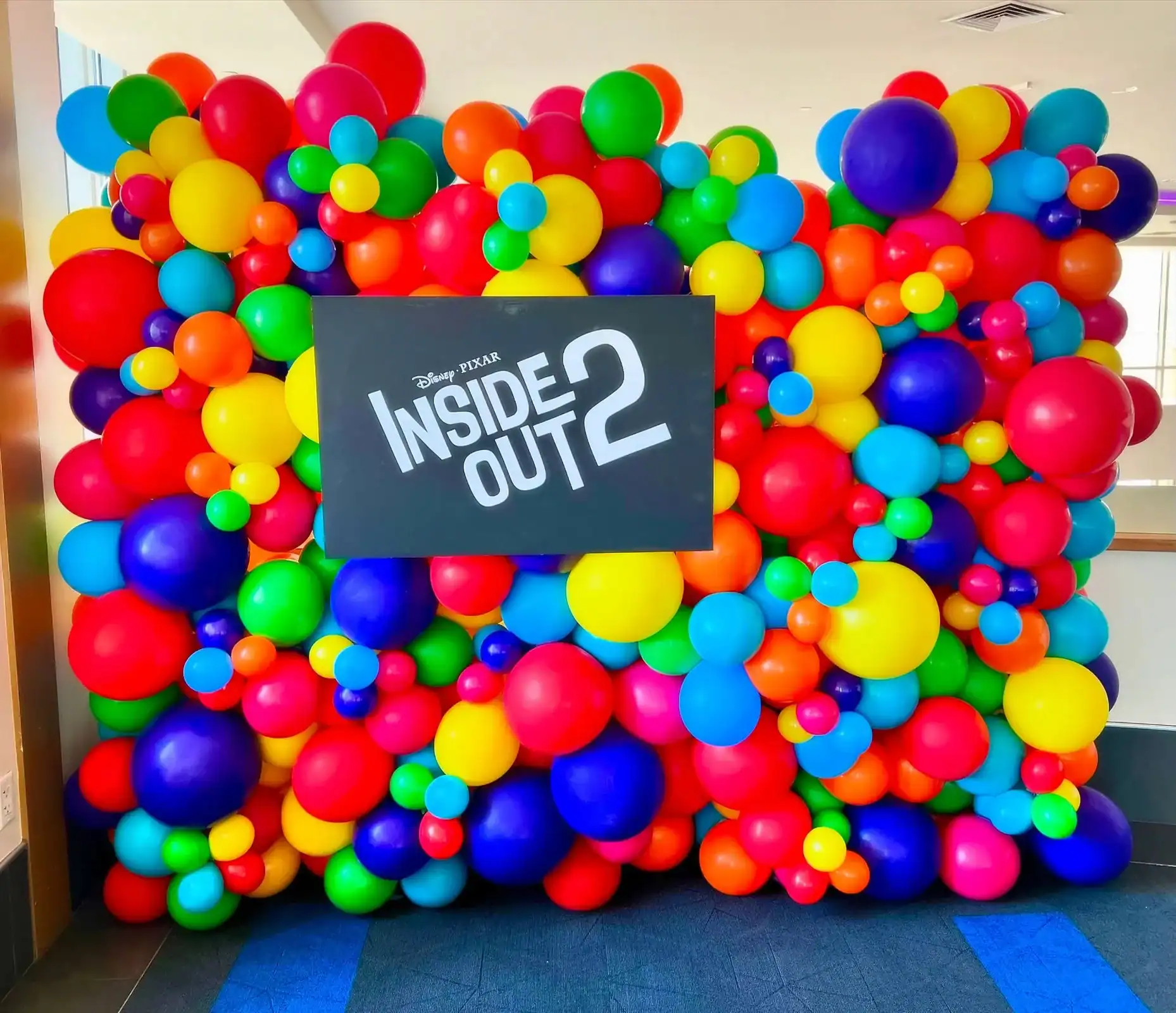A colorful balloon wall with stunning balloon decor and a black sign displaying the Disney Pixar "Inside Out 2" logo in the center.