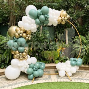 The Balloon Circle Frame, adorned with clusters of white, gold, and green balloons, creates a stunning outdoor display among lush plants and trees in Los Angeles.