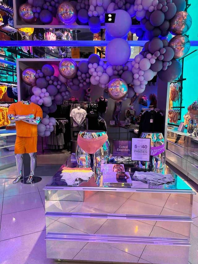 A retail store display in Los Angeles features iridescent mannequins with underwear, surrounded by vibrant balloon installations and promotional signs under bright, colorful lighting.