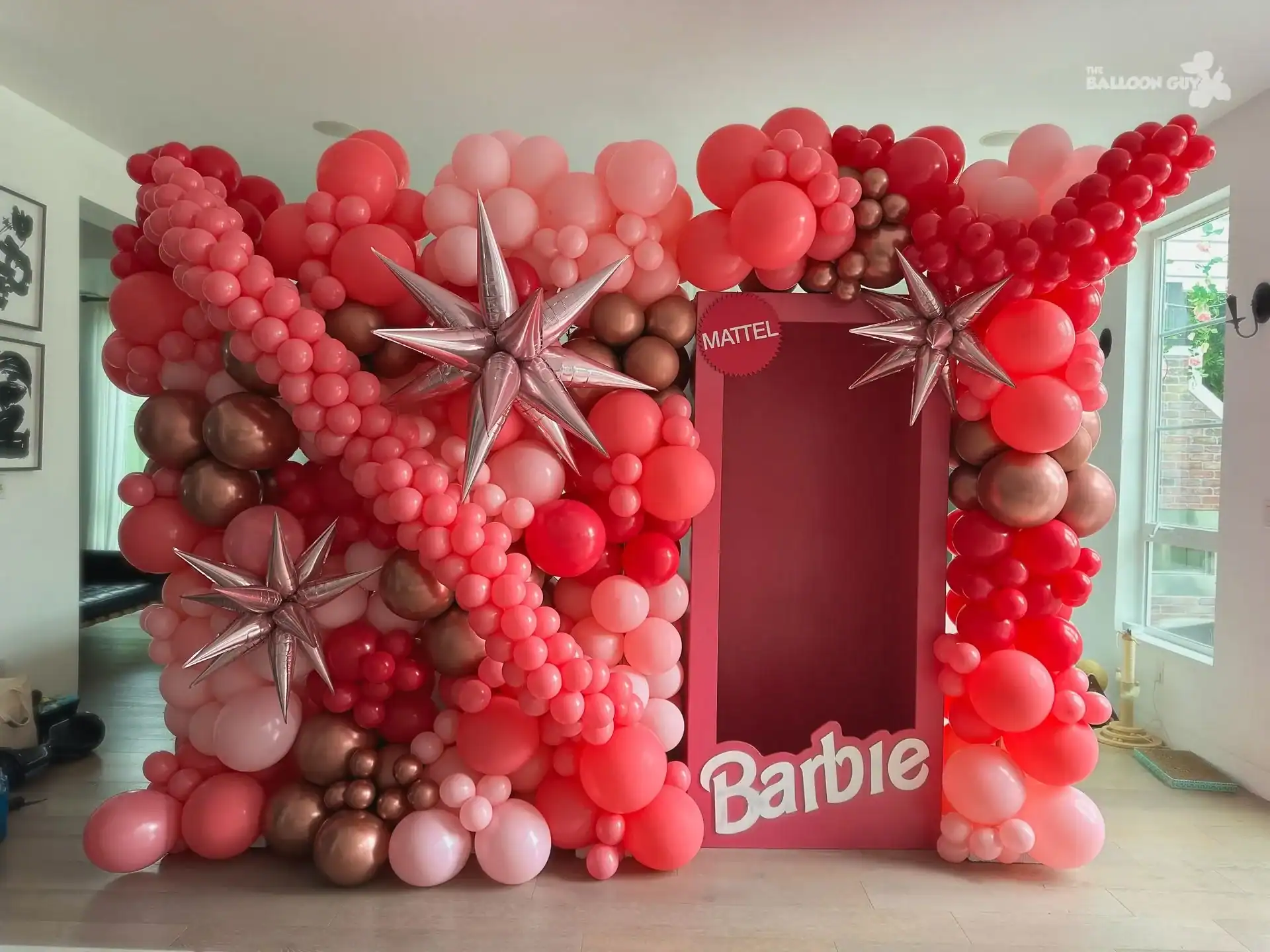 A Barbie-themed photo booth for your corporate event in Los Angeles, decorated with pink, red, and rose gold balloons, metallic star balloons, and a large cutout labeled "Barbie" and "Mattel.