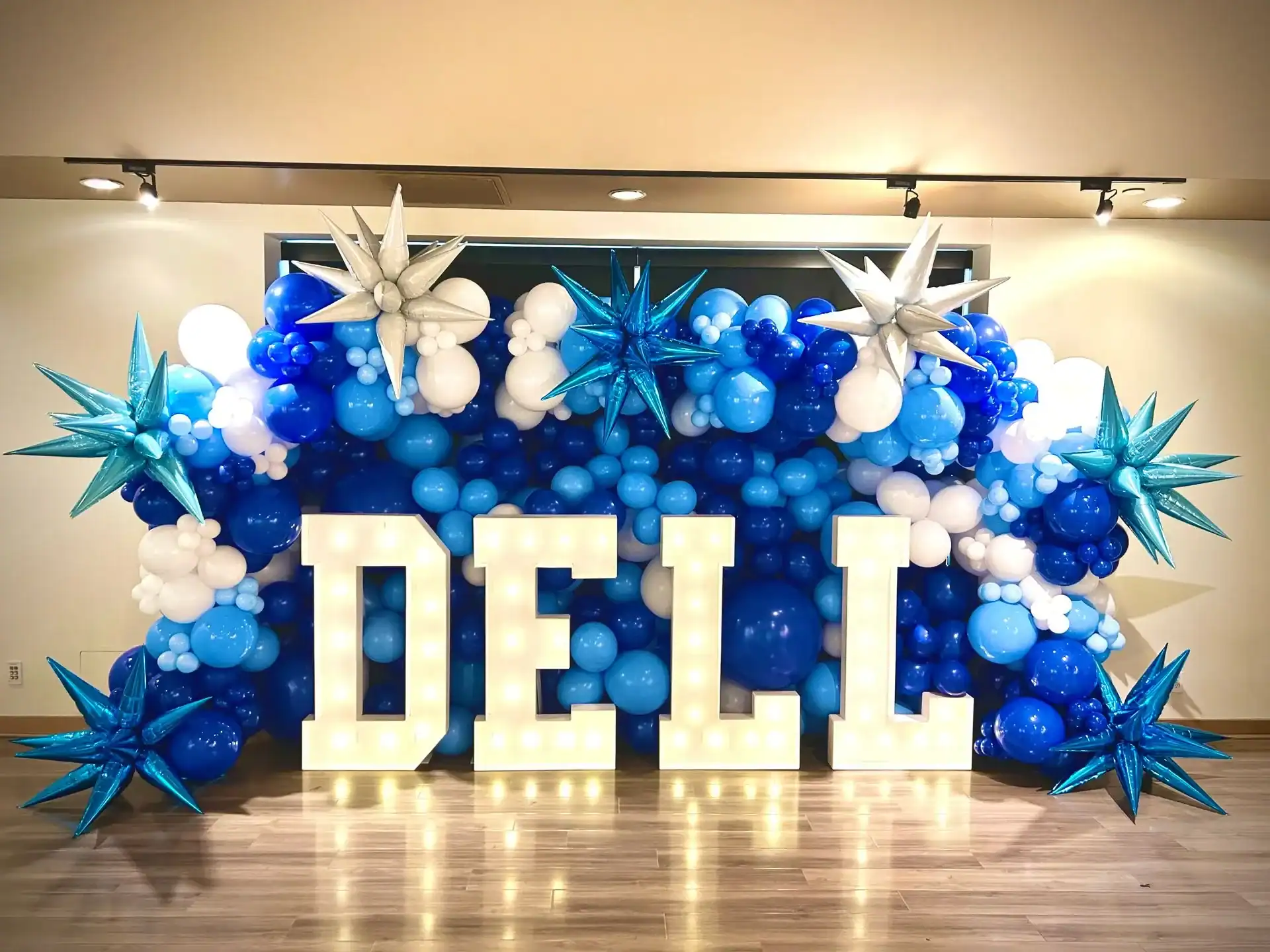 Large lit-up letters spelling "DELL" are displayed in front of blue, white, and silver balloons with star-shaped decorations at a corporate event in Los Angeles.