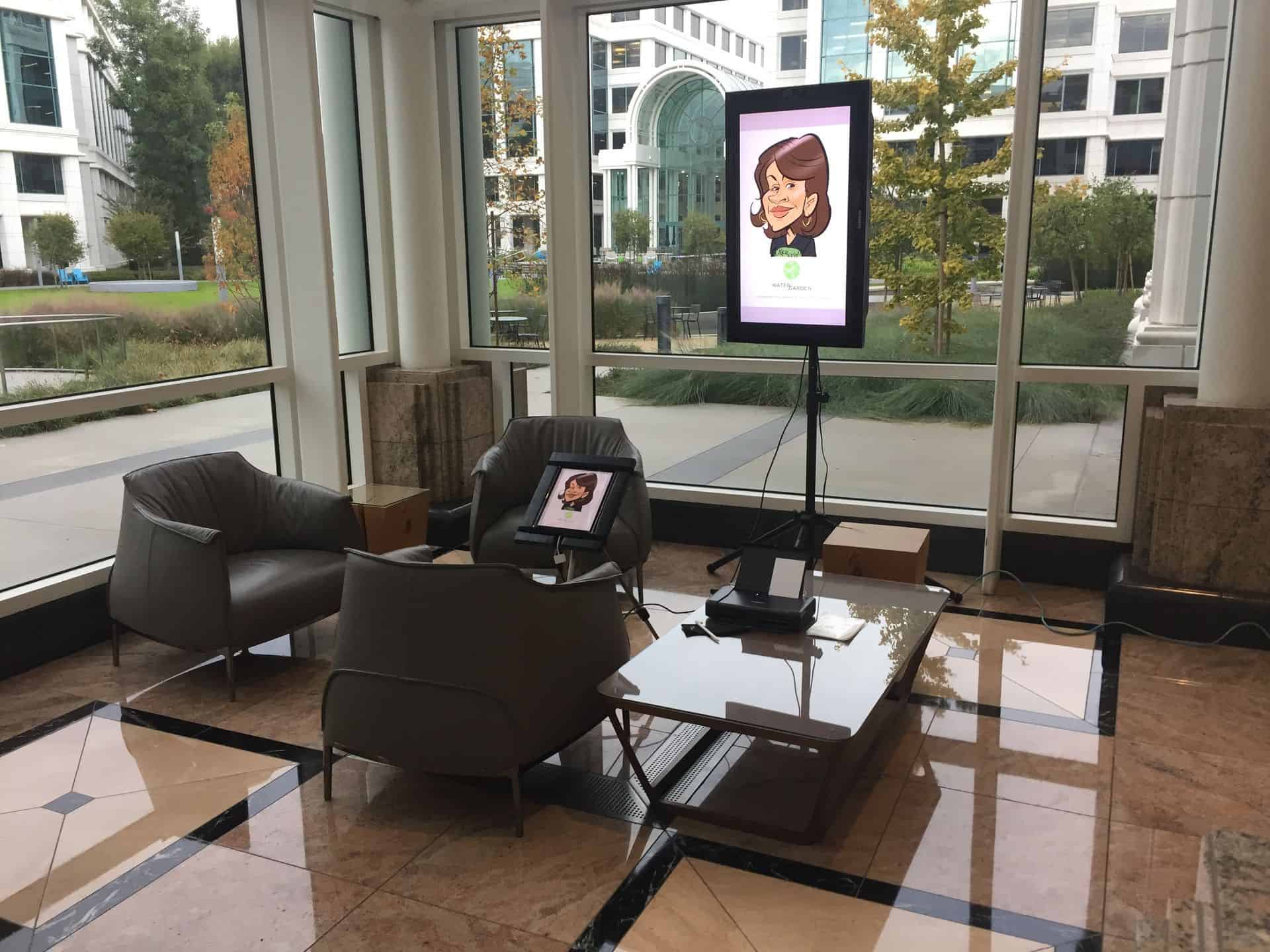 A small lounge area with two chairs and a table sits by large windows at a corporate event in Los Angeles; a digital screen displays a cartoon woman's face above a device on the table.