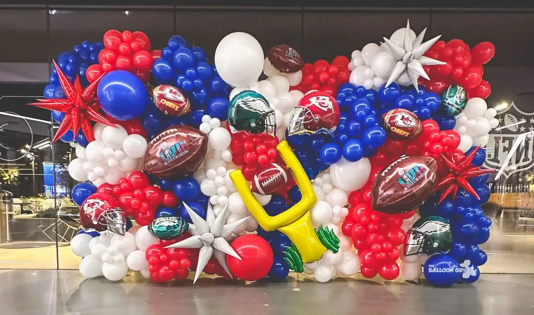 A balloon decor display in red, white, and blue with footballs, goalposts, and helmets, arranged to celebrate the Super Bowl.