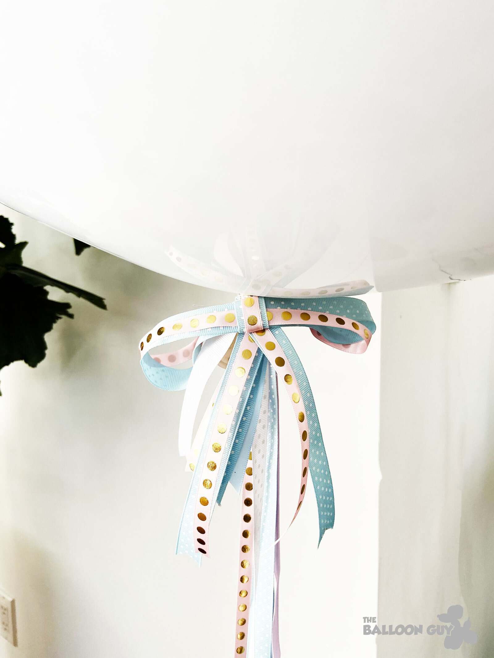 A large white balloon, tied with pastel-colored ribbons featuring gold dots, is positioned near a white wall—perfect for chic Los Angeles events or as part of creative balloon installations by a skilled balloon artist.