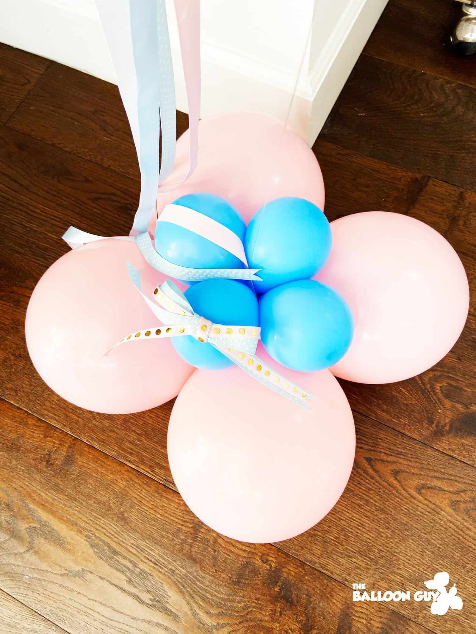 A cluster of pink and blue balloons arranged in a flower shape with ribbon streamers, this unique balloon installation brightens up a dark wooden floor.