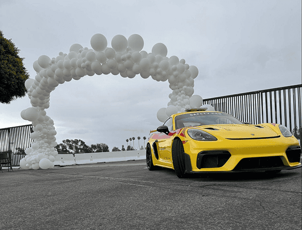 A yellow sports car is parked in front of a large arch made of white balloons, crafted by a talented balloon artist, on a cloudy day.