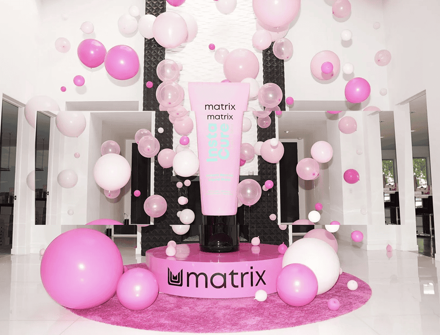 A large pink Matrix hair care product is displayed on a circular platform surrounded by stunning balloon decor in a modern, bright room—perfect for a chic corporate event in Los Angeles.