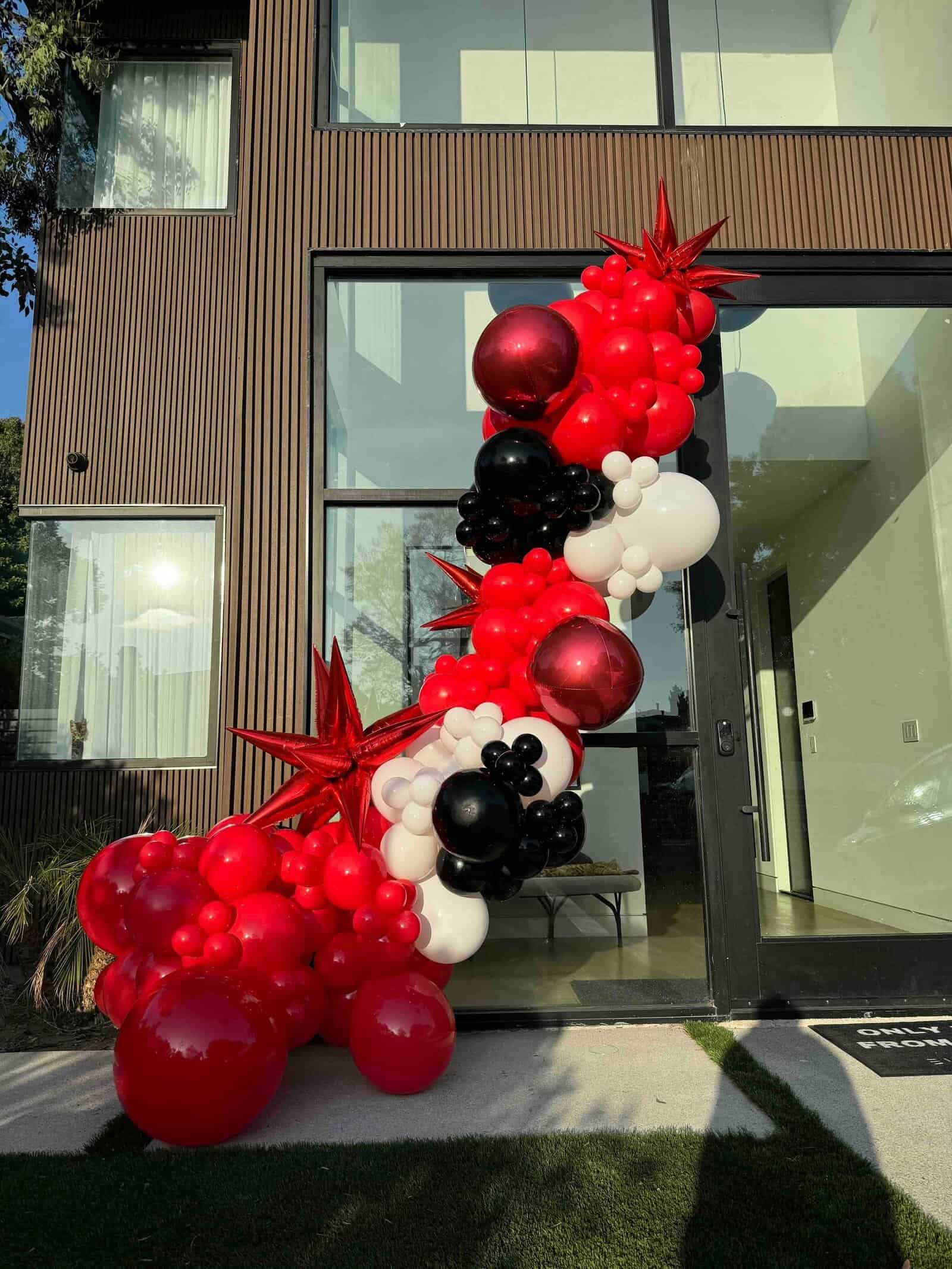 A stunning balloon installation in red, black, and white decorates a modern building entrance for a corporate event, featuring large star-shaped balloons and elegant balloon clusters.