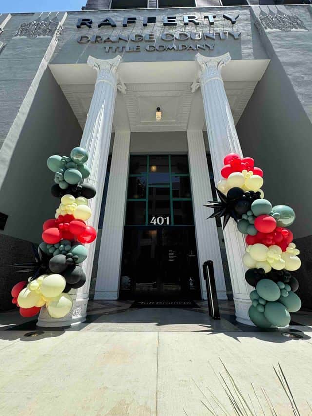 Two white columns at a building entrance feature striking balloon installations, with clusters of red, black, yellow, and green balloons. The address number 401 appears above the door.