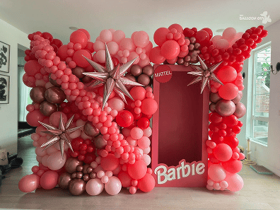 A Barbie-themed photo booth backdrop in Los Angeles, decorated with clusters of pink, red, and metallic balloons, plus large silver star balloons—perfect for any corporate event.