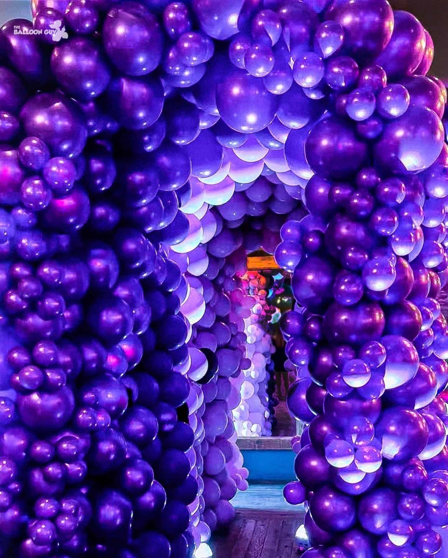 A hallway in Los Angeles decorated with arches made of clusters of purple and lavender balloons, creating a tunnel-like effect and showcasing stunning balloon installations.