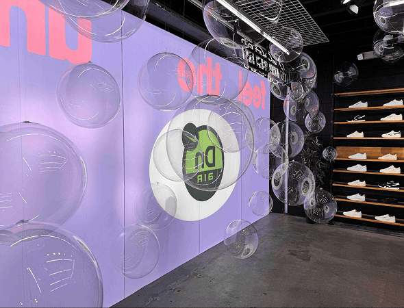 A sneaker store interior features clear balloon decor hanging from the ceiling, a purple wall display with the "Dn Air" logo, and shelves of white shoes—perfect for inspiring your next corporate event.