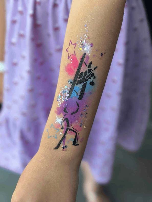 A child's forearm features a painted black giraffe head with pink, purple, and blue background, glitter, and star accents—perfect inspiration for a corporate event with whimsical balloon decor. The child wears a lavender dress.