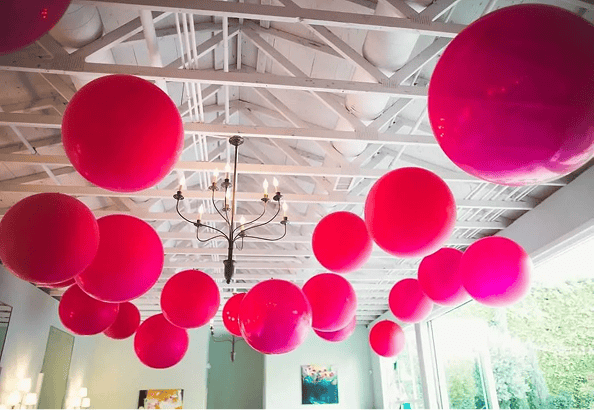 Large pink balloons are suspended from a white ceiling with exposed beams and a black chandelier, creating a striking centerpiece for a bright, modern Los Angeles corporate event.