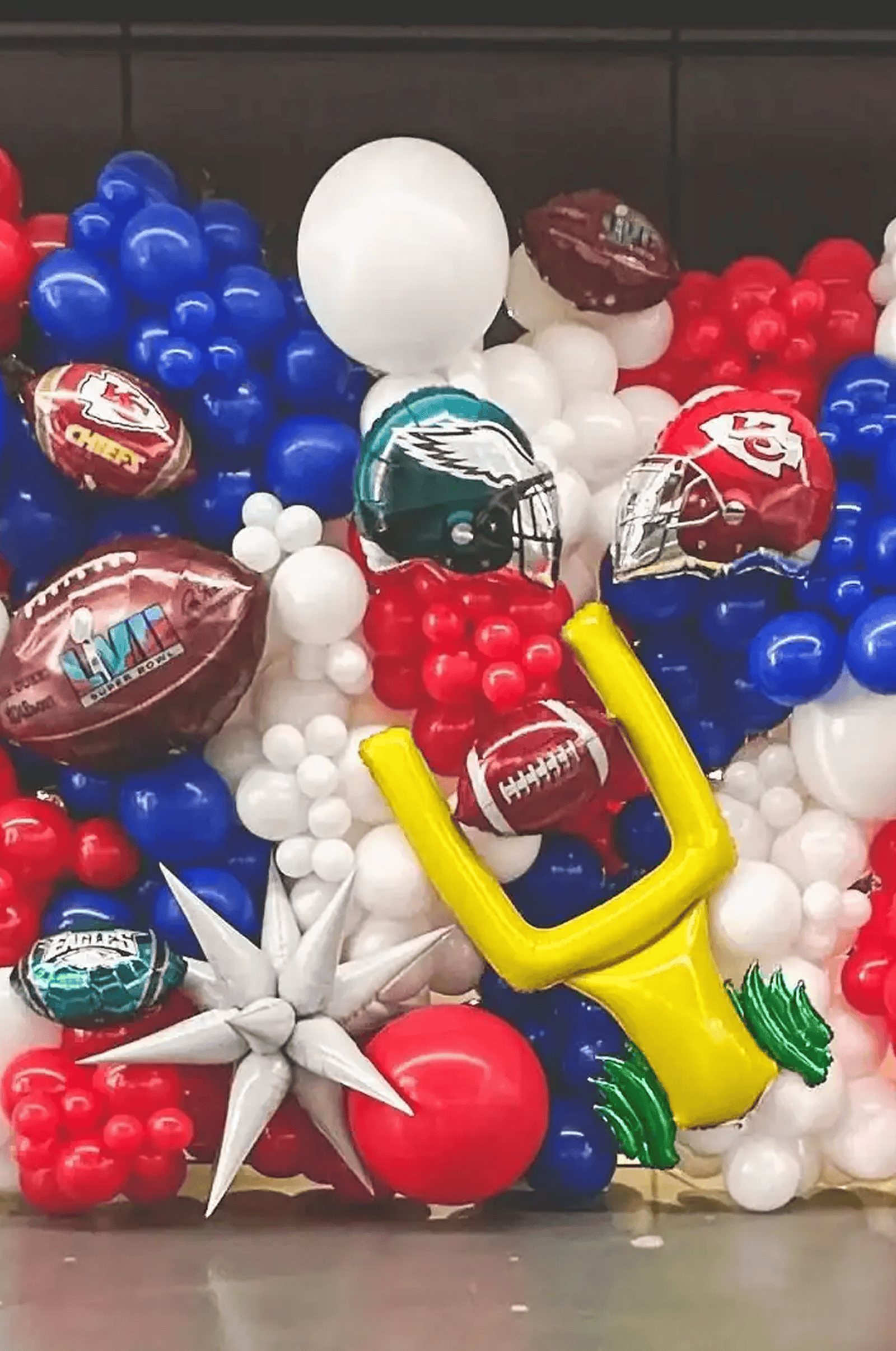 Patriotic balloon decor in red, white, and blue features footballs, helmets, a yellow goalpost, and NFL team logos like the Chiefs and Eagles—perfect party decoration for a Super Bowl celebration.