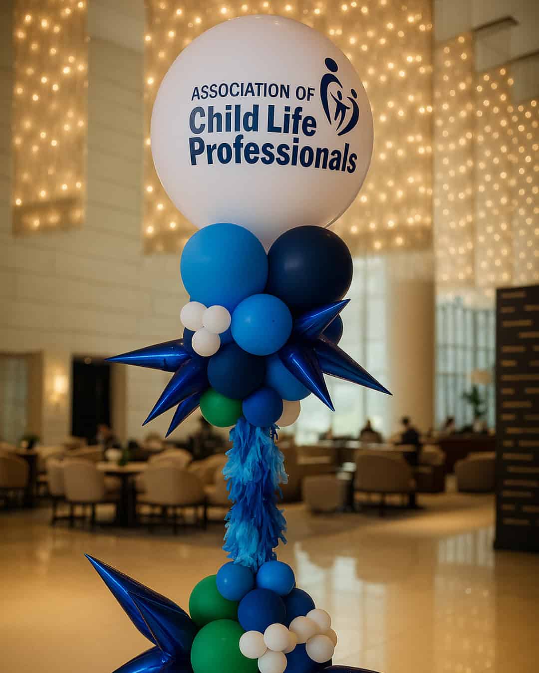 A balloon arrangement with the text "Association of Child Life Professionals" stands in a modern, well-lit lobby, setting a festive tone perfect for Grand Openings as people are seated in the background.