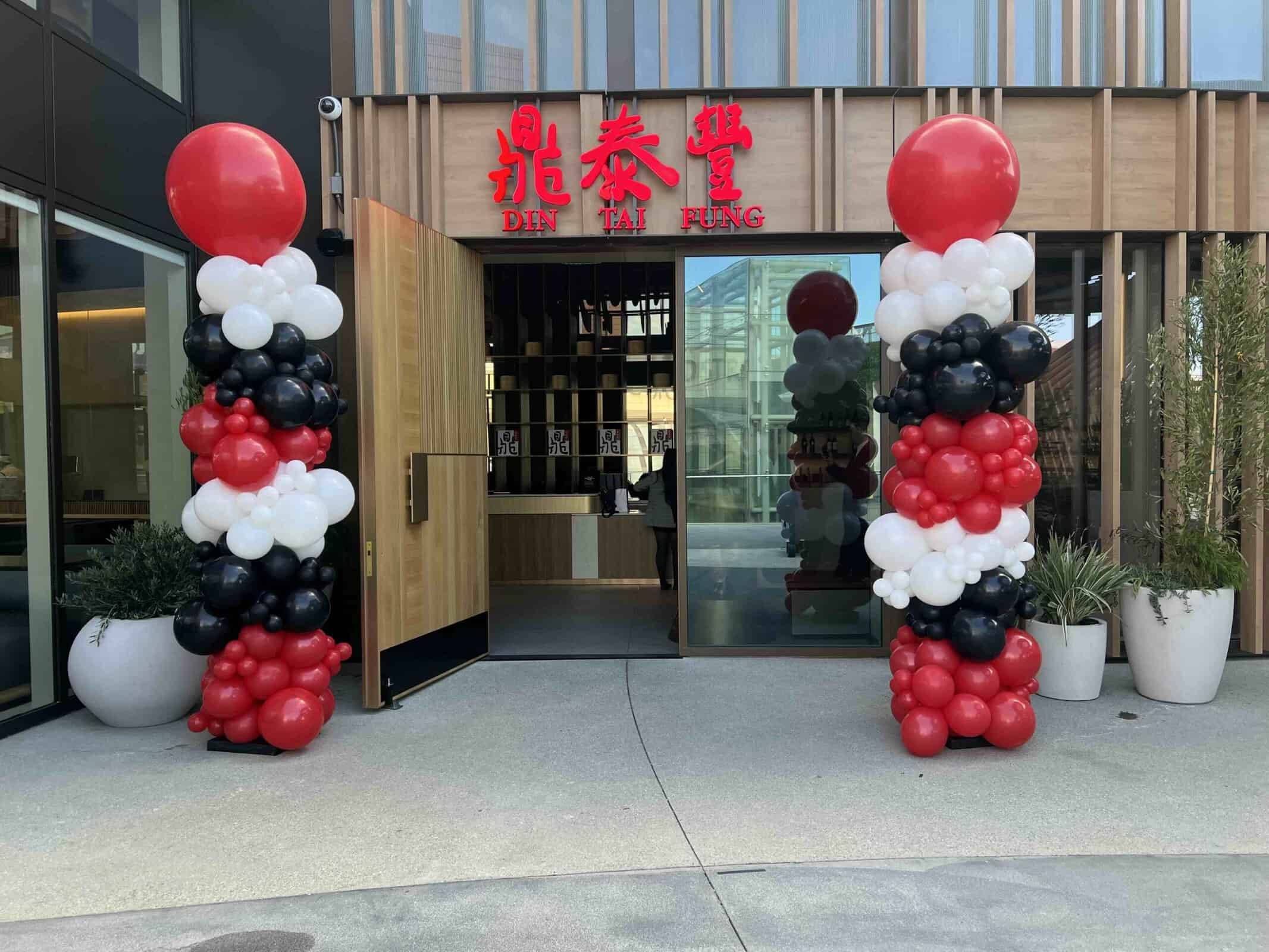 Entrance of Din Tai Fung restaurant adorned with striking balloon columns in red, black, and white on either side of the open door.