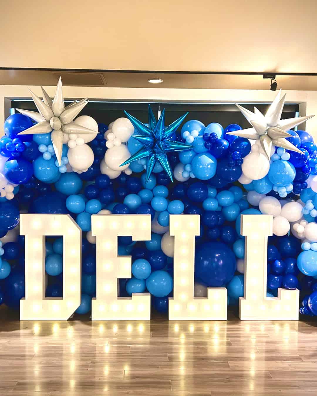 Large illuminated letters spelling "DELL" stand before a blue and white balloon wall with three star-shaped decorations on top, creating a festive display perfect for Grand Openings.