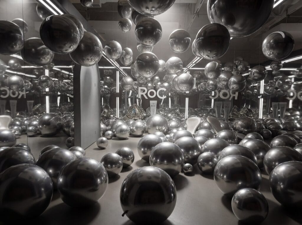 A room filled with reflective silver spheres of various sizes, surrounded by mirrored walls and bright lights, creating multiple reflections—an inspired setting perfect for memorable corporate events.