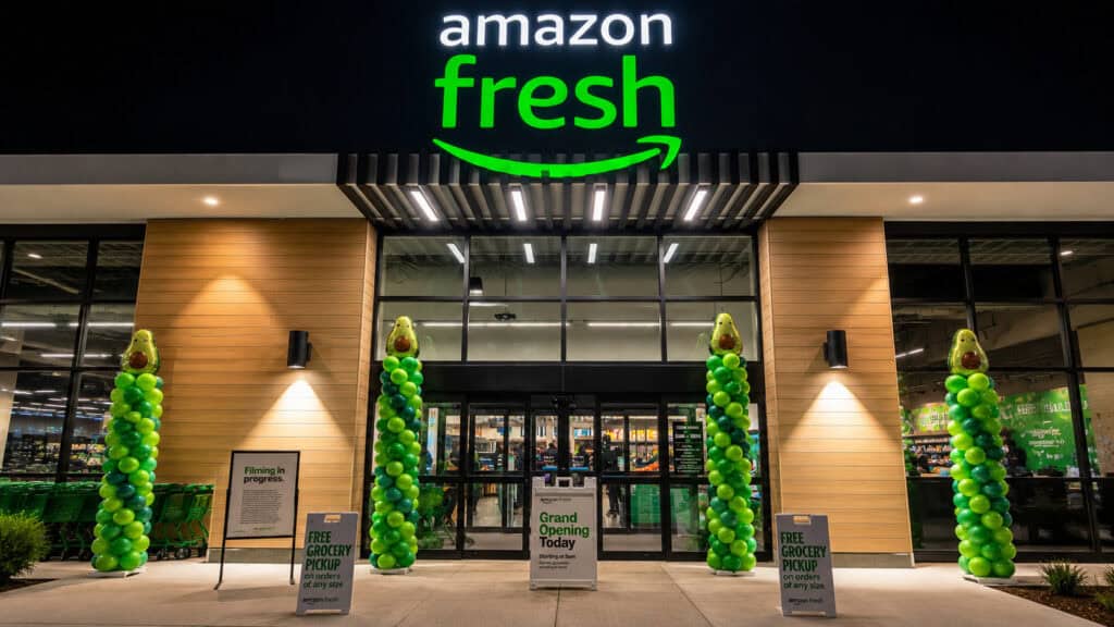 Amazon Fresh grocery store exterior at night with custom balloon columns in vibrant green and grand opening signs welcoming customers at the entrance.