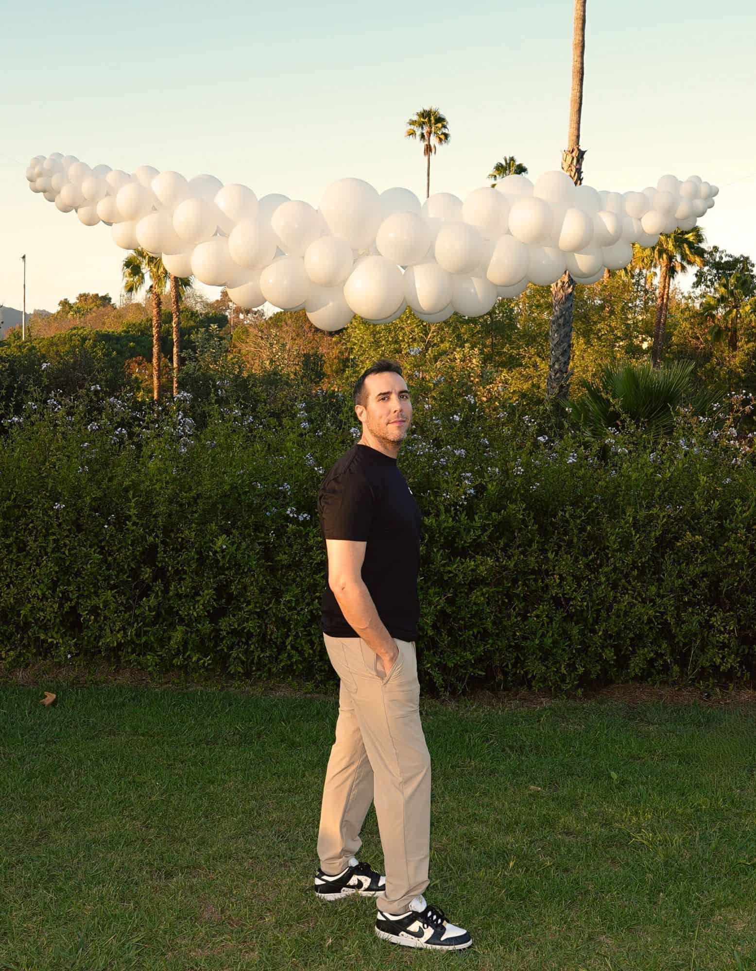 Celebrity balloon stylist, Sean Edwards, is standing in front of a cloud made of balloons.